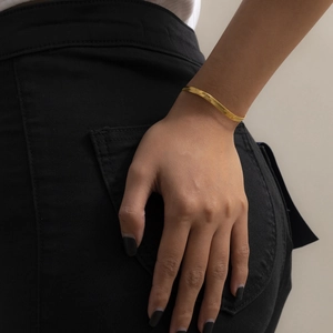 Nahaufnahme eines goldenen flachen Schlangenkette-Armbands am Handgelenk einer Frau