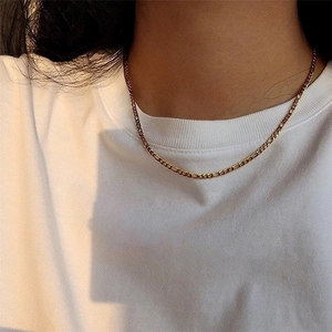 Detail of gold-plated stainless steel Figaro chain necklace on model with soft lighting