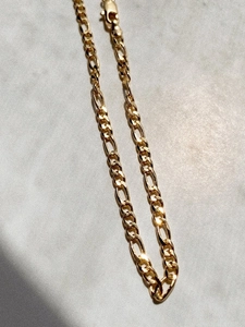 Detailed close-up of golden Figaro chain necklace with lobster clasp and mirror finish