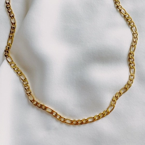 Detailed close-up of polished gold Figaro chain links on a white silk background