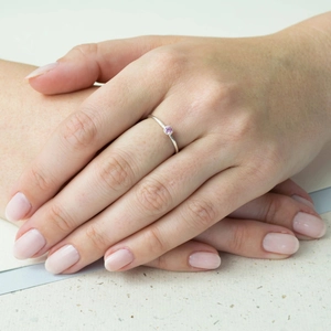 Detail of a minimalist silver ring with a small pink zircon gemstone on a model's hand