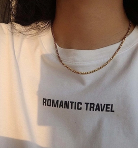 Close-up of a 18K gold plated Figaro chain necklace on a model wearing a white tee