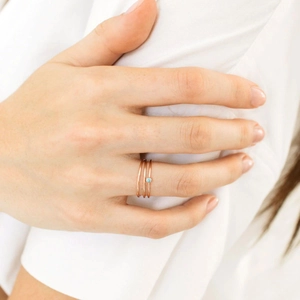Three-piece rose gold minimalist rings stacked on a finger with a small blue zircon gem