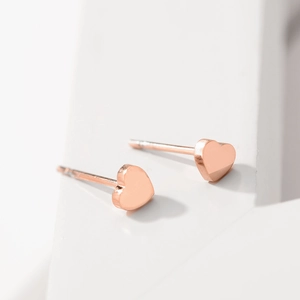 Gros plan de boucles d'oreilles cœur en or rose sur un bloc de pierre géométrique blanc