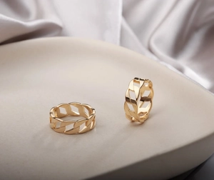 Macro detail of gold plated stainless steel Cuban link rings on cream ceramic tray