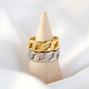 Close-up of gold and silver Cuban link chain rings on a wooden stand with satin background