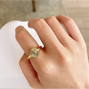 Macro shot of gold-plated sunburst textured ring worn on index finger with glossy finish