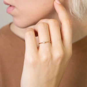 Detail of a minimalist rose gold stainless steel ring with a round zircon on a model finger