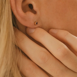 Gros plan d'une puce d'oreille plaquée or avec une pierre précieuse violette facettée