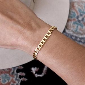 Detailed view of a gold-plated Cuban link bracelet worn on wrist with elegant accessories