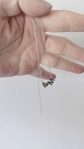 Collier en acier inoxydable argenté avec pendentif cœur et lettre M tenu à la main