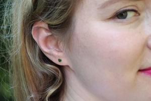 Gros plan de boucles d'oreilles cœur minimalistes en métal sombre portées par un modèle