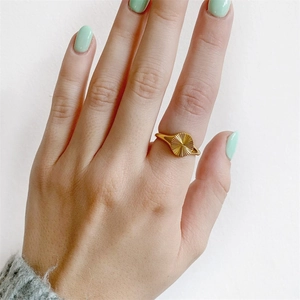 Close-up of a gold signet ring with sunburst texture worn on finger with green nails