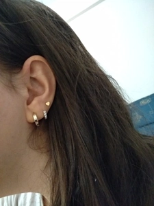 Détail macro de boucles d'oreilles cœur doré et créoles à cristaux sur l'oreille