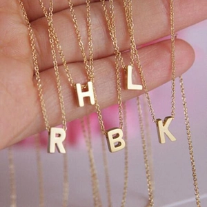 Détail de colliers dorés avec pendentifs cœur et lettre tenus à la main sur chaîne O