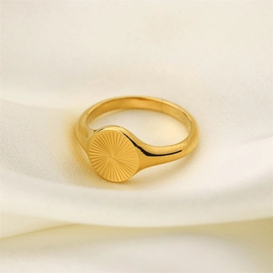 Close-up of a gold-plated stainless steel ring with sunburst texture on white silk