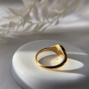 Close-up of a minimalist gold signet ring with a polished mirror finish on a white tray