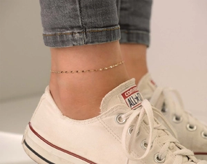 Nahaufnahme einer vergoldeten Edelstahl-Fußkette getragen mit Freizeitschuhen