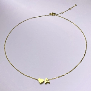 Détail d'un collier doré avec pendentifs cœur et lettre A sur un fond clair uni