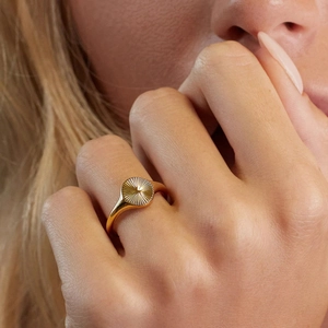 Detail of gold plated signet ring with radial sunburst texture on model finger