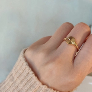 Detail of gold sunburst engraved signet ring worn with a beige knitted sweater