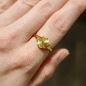 Macro shot of gold signet ring featuring radiant sunburst texture on a round face