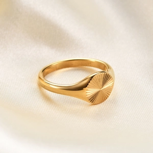 Macro view of gold plated signet ring featuring sunburst engraving on champagne silk