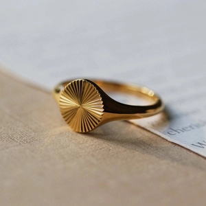 Macro shot of gold sunburst engraved signet ring on a textured book background