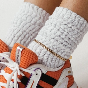 Detailed view of a trendy golden Cuban chain anklet worn over white knitted socks