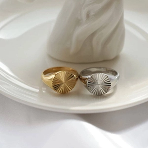 Detailed view of two sunburst pattern signet rings in gold and silver on a ceramic tray