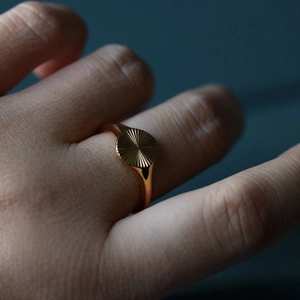 Macro detail of a minimalist gold signet ring featuring a radial sunburst engraving texture