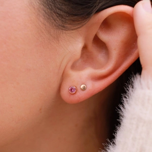 Close-up of pink gemstone and gold round stud earrings worn for a stylish layered look