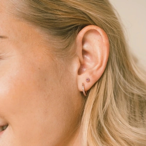 Close-up of pink crystal stud and gold zircon hoop earring worn by a model