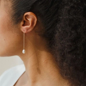 Detailed view of long gold chain earrings with drop pearls on a model