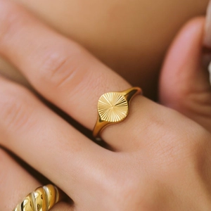 Close-up of golden signet ring with radial sunburst texture and polished finish