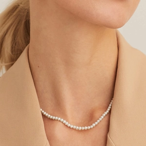 Detailed view of elegant faux pearl necklace worn with a professional beige blazer