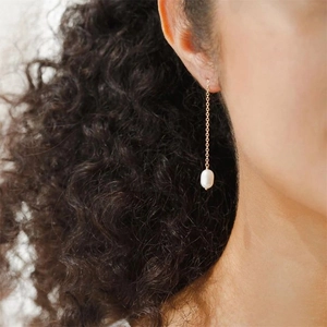 Detail of long gold chain earrings with elegant white pearls worn by a model