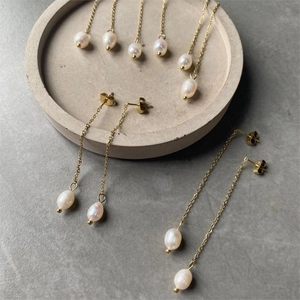 Detail of long chain gold plated earrings featuring hanging white teardrop pearls