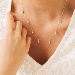 Detail of elegant gold chain necklace with oval pearls worn on a white blouse