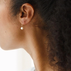 Close-up of minimalist gold chain pearl earrings worn by a model in warm natural light