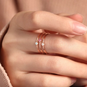 Drei roségoldene Ringe mit blauen, rosa und weißen Edelsteinen auf einem rosa Pullover