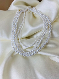 Detail view of multi-layer faux pearl necklace on elegant cream silk fabric background