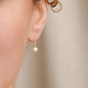 Detail of gold-plated drop earring with a glossy white pearl and fine link chain