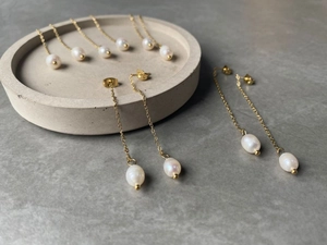Close-up of gold chain earrings with natural baroque pearls on a stone display