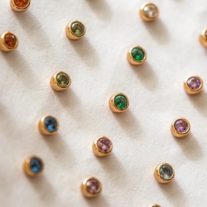 Detail view of colorful birthstone stud earrings in a polished gold bezel setting