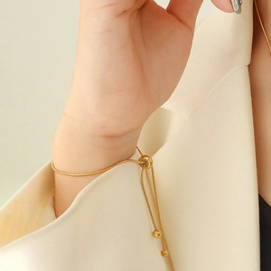 Close-up of a gold adjustable snake chain bracelet with a draw-string ball clasp on a wrist