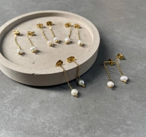 Detailed view of long gold chain pearl drop earrings elegantly displayed on a grey tray