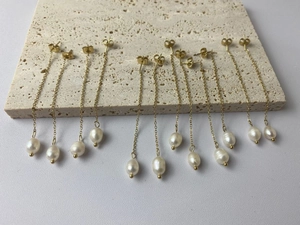 Detail shot of long gold chain earrings with white baroque pearl drops on a beige stone