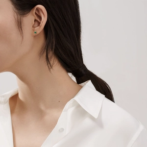 Close-up of a minimalist round green crystal stud earring worn by a model in gold finish
