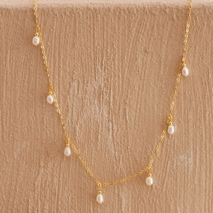 Detail view of golden stainless steel necklace with seven teardrop white pearls on stone